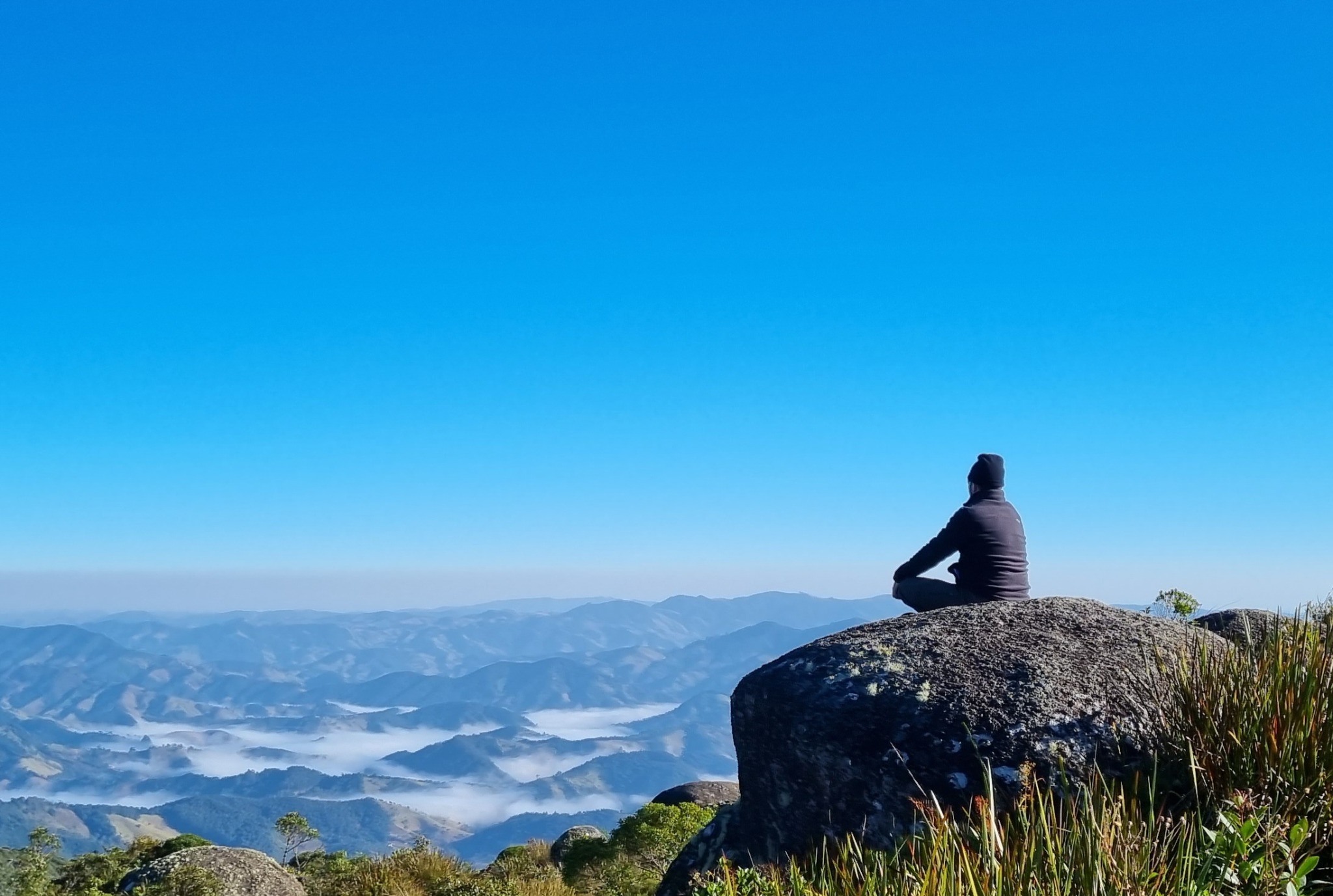 Cristiano sentado sobre uma pedra, contemplando uma paisagem de montanhas e vales cobertos por nuvens.